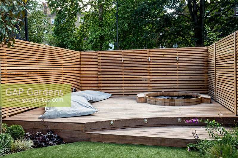 Jardin contemporain entouré d'un treillis en treillis de cèdre pour plus d'intimité autour d'une terrasse en bois en escalier avec bain à remous et grands coussins de salon de jardin