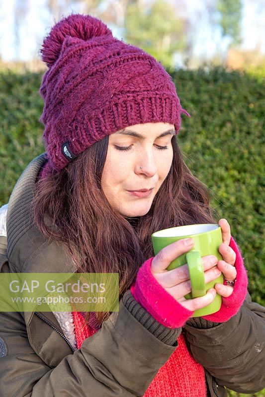 Femme soufflant sur une tasse de boisson chaude dans le jardin.