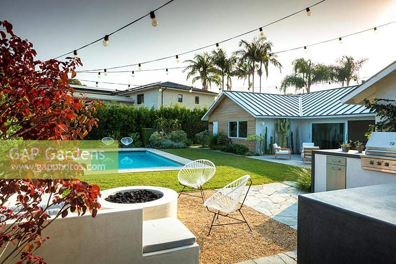 Vue sur le jardin avec des guirlandes lumineuses pour la piscine et le coin salon extérieur. Jardin conçu par Falling Waters Landscape, inc Ryan Prange, New Port Beach, Californie, USA.