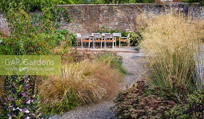 Admirez les plates-bandes mixtes de plantes vivaces et d'herbe dans le jardin contemporain jusqu'à la table et les chaises. Conception du jardin Elks-Smith.