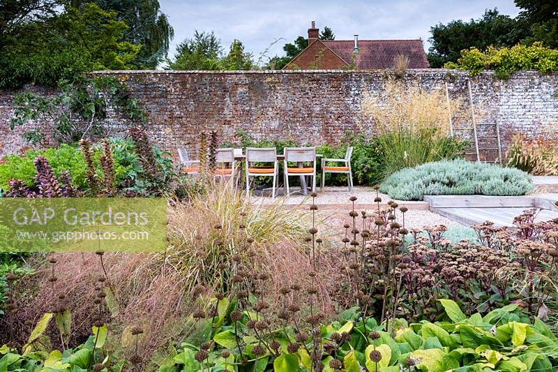 Vue sur parterre de fleurs mélangé à table et chaises d'extérieur dans un jardin de campagne contemporain près de Winchester, Hants, Royaume-Uni. Conception du jardin Elks-Smith.