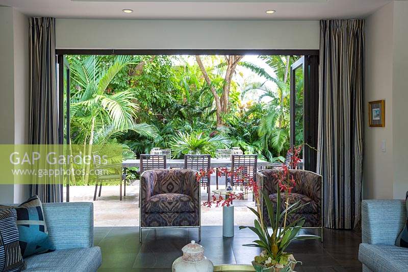 Vue de l'intérieur de la maison, à travers des portes ouvertes sur le patio du jardin et une luxuriante plantation tropicale. Floride, USA. Conception de jardin par Craig Reynolds Landscape Architecture.