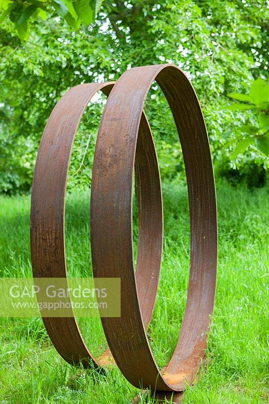 Moongates - cercles d'acier doux - dans l'herbe avec des arbres au-delà