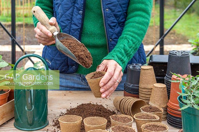 Femme remplissant des pots biodégradables avec du compost à l'aide d'une cuillère.