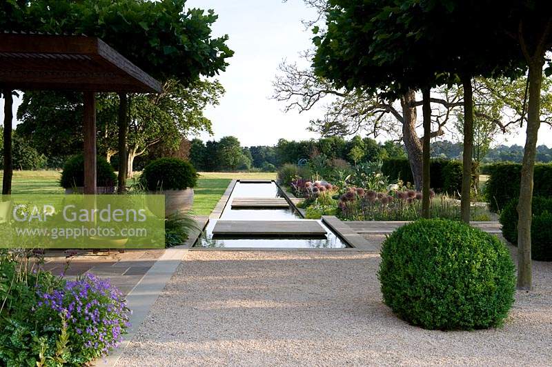 Vue sur une piscine étroite dans un jardin contemporain, avec des terrasses pavées.