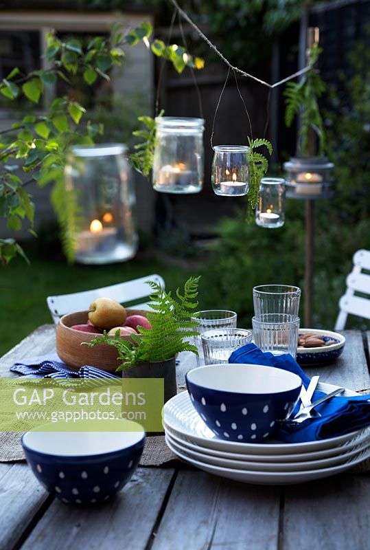Lanternes de pot de confiture avec des bougies suspendues au fil suspendu au-dessus de la table de jardin.
