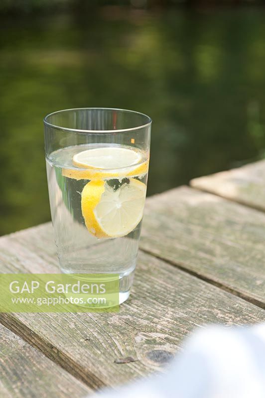 Un verre d'eau citronnée sur une terrasse en bois à côté d'un ruisseau.