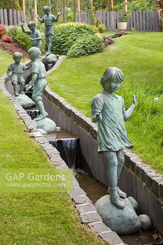 Figures en bronze d'enfants jouant dans une rainure en ardoise sur une pelouse en pente