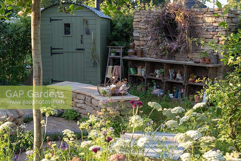 Un jardin de campagne romantique planté principalement de plantes médicinales, une cabane de berger, un banc de pierre incurvé et une exposition éclectique d'objets. Le jardin Naturecraft, conçu par Pollyanna Wilkinson, RHS Hampton Court Palace Garden Festival, 2019.