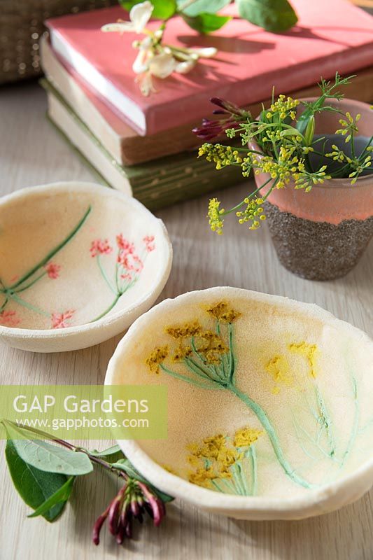 Petits bols, en pâte à sel et décorés d'empreintes de fleurs peintes, sur une table avec des livres et des fleurs fraîches