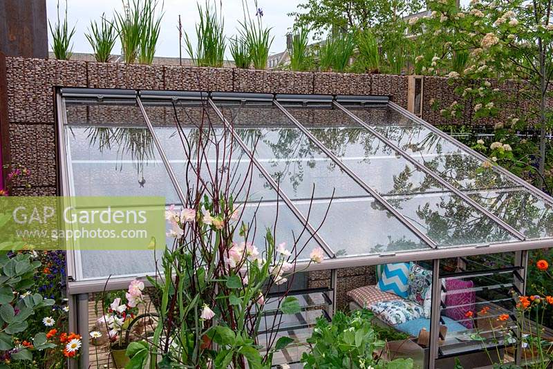 Serre adossée engloutie à côté d'un mur de gabions - Le jardin des enfants du centenaire Montessori, RHS Chelsea Flower Show 2019