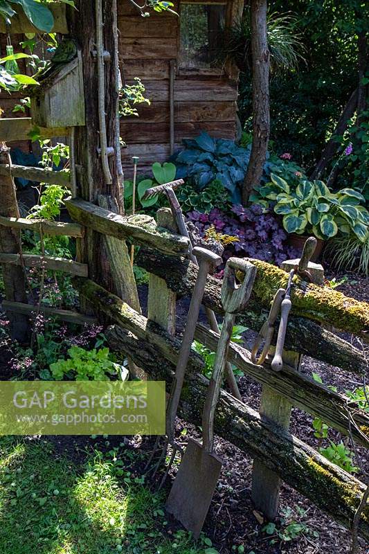Vieux outils de jardin s'appuyant sur une clôture rustique moussue