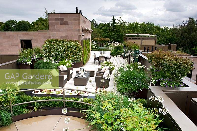 Vue sur le jardin sur le toit urbain et contemporain, montrant la disposition des différents sièges et la plantation sur les murs, les parterres de fleurs et les pots
