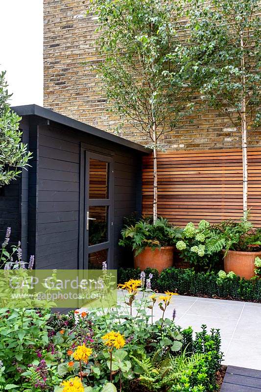 Salon de jardin en bois noir dans petit jardin londonien contemporain avec treillis en lattes de cèdre.