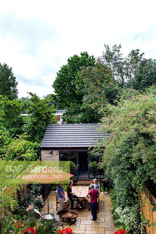Vue élevée du jardin contemporain dans l'ouest de Londres avec terrasse en pierre, salon de jardin et parterres de fleurs herbacées. Les propriétaires discutant avec Nick Gough, l'un des designers.