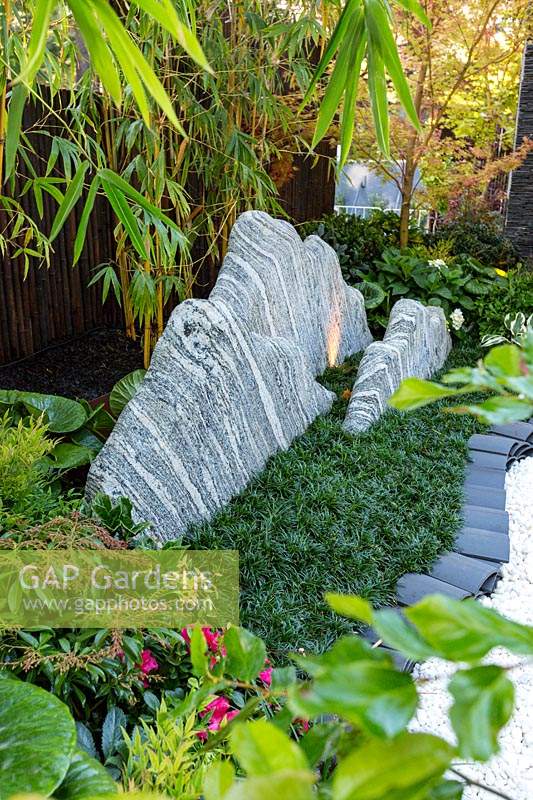 Les roches grises et blanches à rayures sont censées symboliser une chaîne de montagnes dans un jardin entouré d'une couverture végétale plantée sur l'herbe Mondo naine, le jardin est bordé de toits chinois incurvés gris.