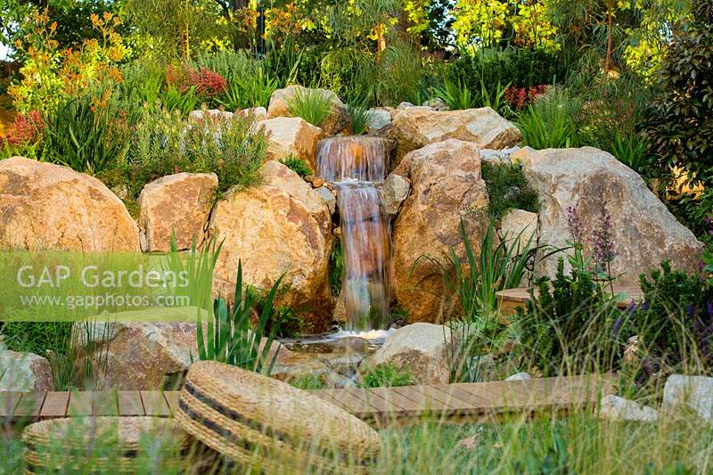 Une cascade d'aspect naturaliste faite de roches de grès rustique et plantée d'une variété d'arbustes et d'herbes
