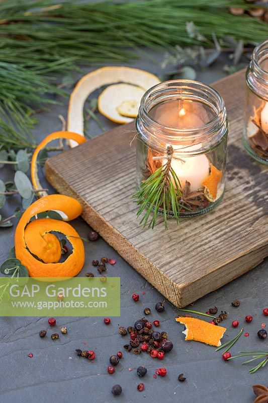 Bougies parfumées à base d'épices, d'écorces d'orange, de pin et de bougies placées dans un pot de confiture sur une planche de bois