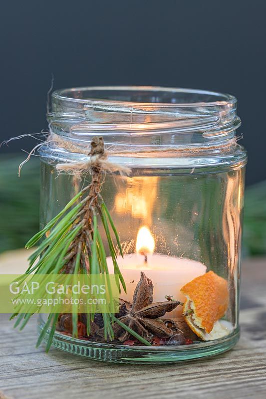 Bougies parfumées à base d'épices, d'écorces d'orange, de pin et de bougies placées dans un pot de confiture sur une planche de bois