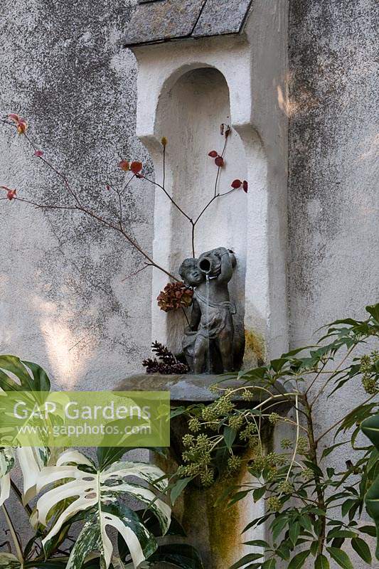 Petite statue comme fontaine murale, entourée de feuillage tropical