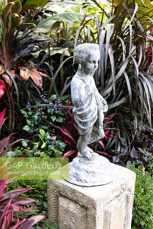 Feuillage tropical entourant la statue de chérubin sur socle, chérubin a chrysalide monarque accroché à une oreille