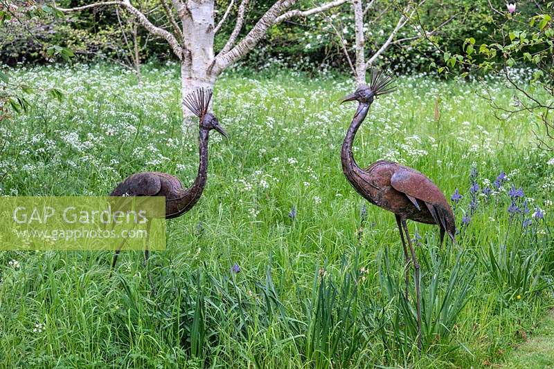 Deux sculptures d'oiseaux en métal dans un pré de fleurs sauvages.