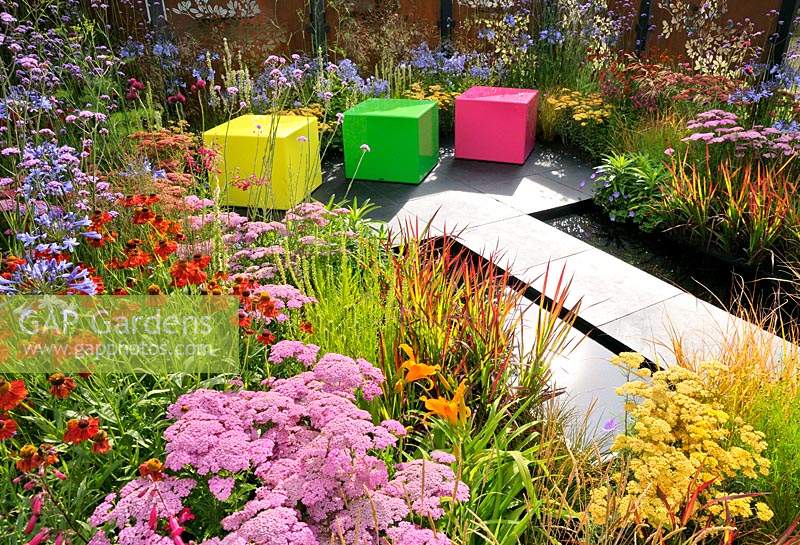 Jardin Color Box, RHS Hampton Court Palace Flower Show, 2017. Parterres de fleurs vivaces colorés avec chemin de calcaire et sièges en plastique.