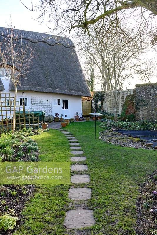 Chemin en pierre à travers Cottage Garden menant à chaumière en février.