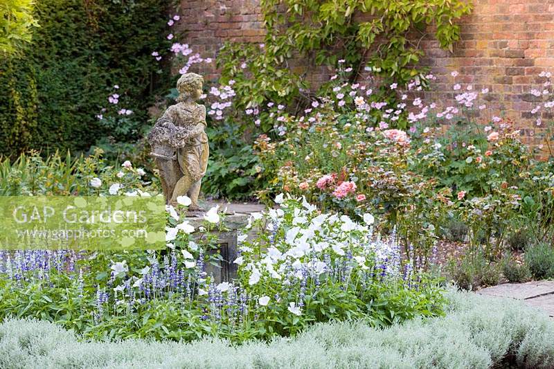 Des pétunias et des Salvias annuels sont plantés autour d'une petite statue en pierre dans le jardin du drapeau à Arley Hall, Cheshire, Royaume-Uni.