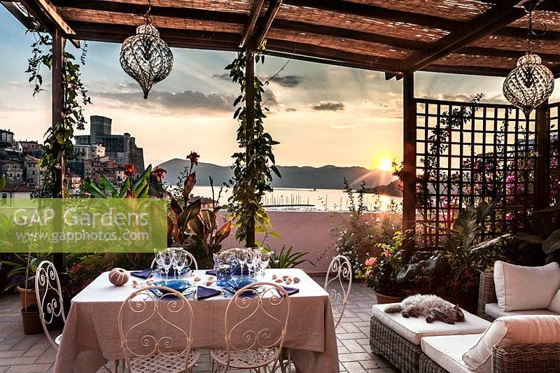 Salon et salle à manger en plein air sur terrasse avec vue sur le château et le port de Lerici au coucher du soleil