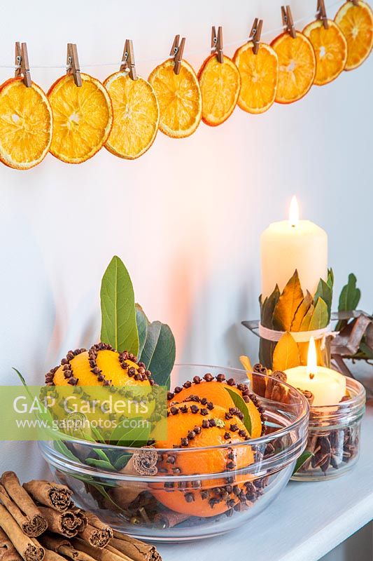 Étagère décorée d'oranges clouées de clous de girofle, de bougies et de Laurus nobilis - Baie, au-dessus de tranches d'orange chevillées en ligne