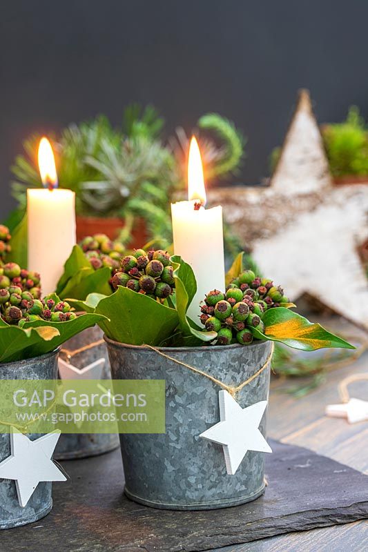 Décoration de table avec des bougies dans des seaux miniatures galvanisés remplis de baies de lierre et de feuilles de laurier