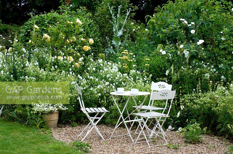 Meubles de style café blanc sur une zone de gravier dans le jardin du chalet.