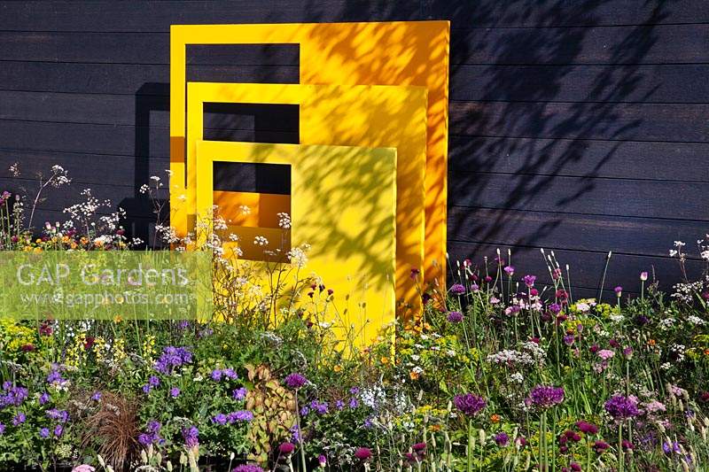 Mur plaqué sombre avec des panneaux sculpturaux en acier jaune et des pings de couleurs vives partout dans 'Urban Oasis' au RHS Malvern Spring Festival 2018