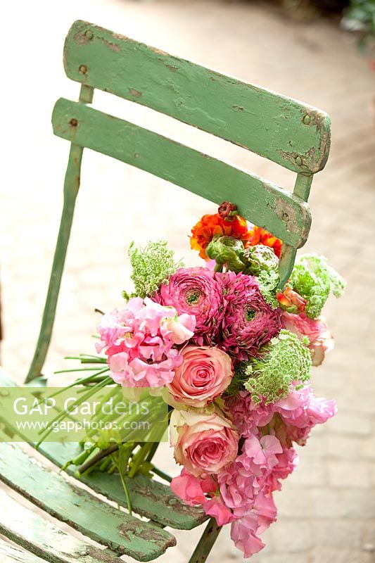 Bouquet de visnaga daucoides, renoncules, pois de senteur et roses sur une chaise en bois