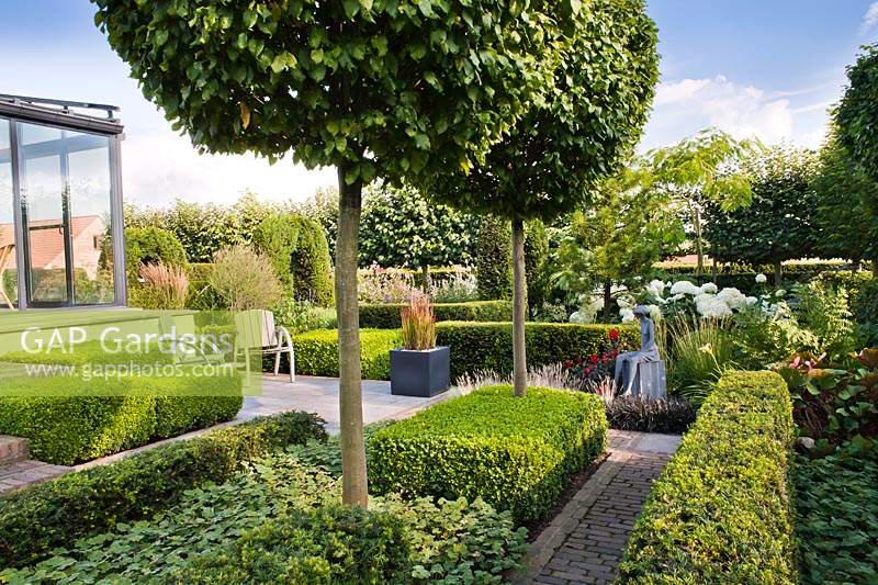 Vue sur le jardin moderne, avec des haies basses et des ifs, Carpinus betulus - Normes topiaires des sucettes charme et un espace de détente.