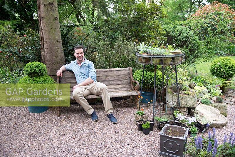 Homme assis sur un banc en bois à l'ombre dans une zone de gravier avec des pots de plantes