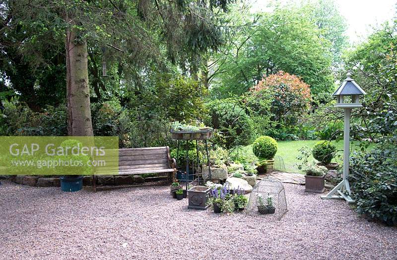 Vue sur un jardin ombragé avec zone de gravier, sièges, pots, topiaire avec pelouse et arbustes
