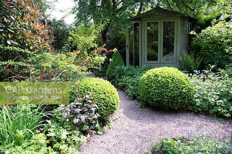 Jardin de la petite ville ombragée avec parterres de fleurs mixtes et Buxus - Boîte - topiaire près du chemin de gravier vers le pavillon d'été