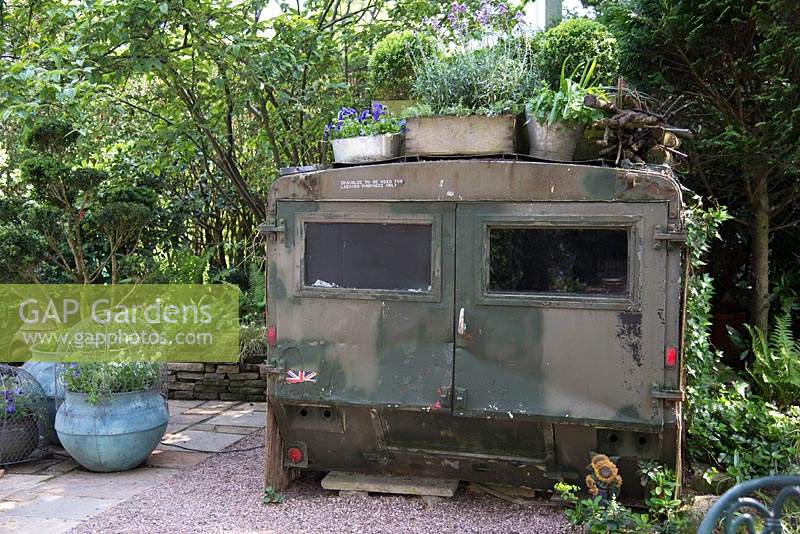Vieux véhicule militaire inhabituel utilisé comme abri dans un petit jardin ombragé