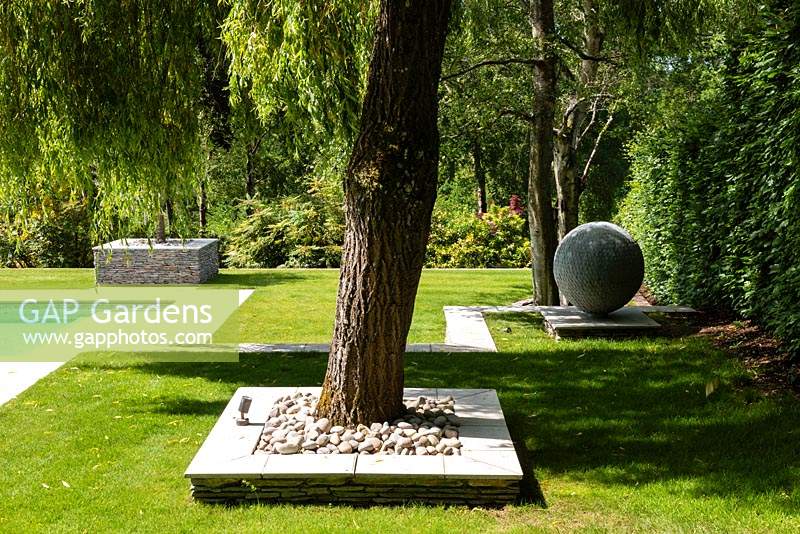 Jardin moderne, vue sur pelouse avec parterre paysager dur autour de spécimen arbre et ornement globe