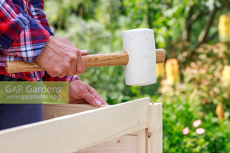 Close up detail de l'utilisation d'un maillet en caoutchouc souple pour insérer des panneaux latéraux en bois dans un bosquet prédécoupé