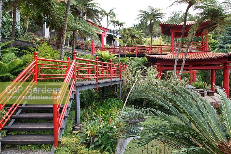 Jardin d'inspiration orientale inférieur avec mains courantes en bois peintes en rouge, situé dans un jardin tropical