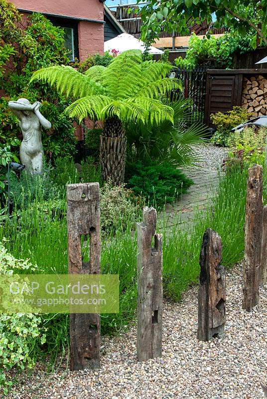 Statue classique à côté de fougère arborescente en parterre de fleurs d'arbustes mixtes, avec de la lavande et des poutres en bois recyclées créant une caractéristique bordant le chemin - Journée des jardins ouverts, Woolpit, Suffolk