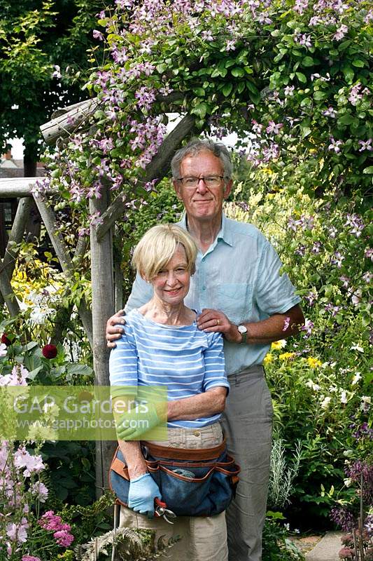 Couple dans leur jardin par grimpeur en fleurs sur un support rustique