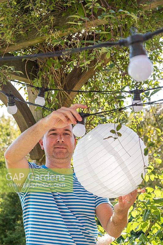 Homme fixant une lanterne en papier blanc sur les ampoules dans la chaîne légère