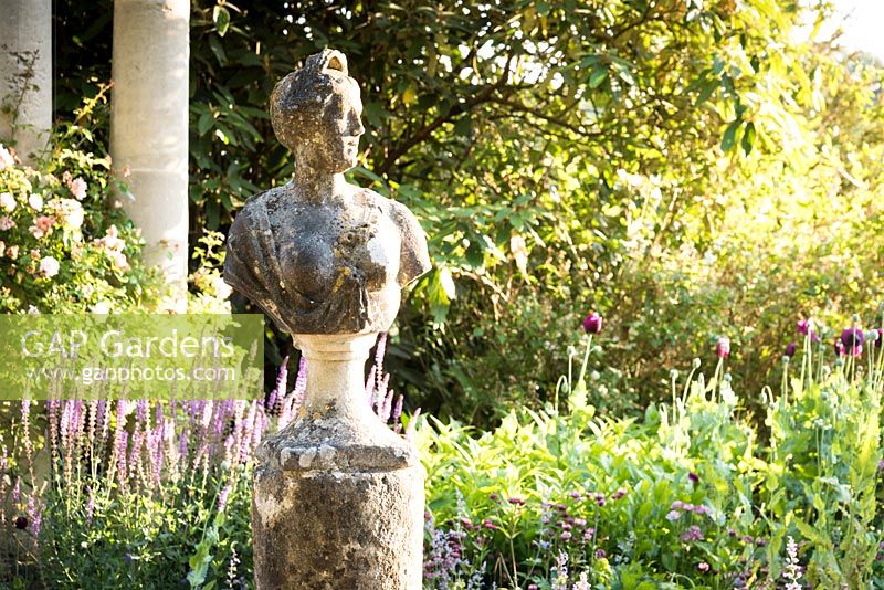 Buste français de femme sur socle et colonne de pierre, parterre de fleurs au-delà