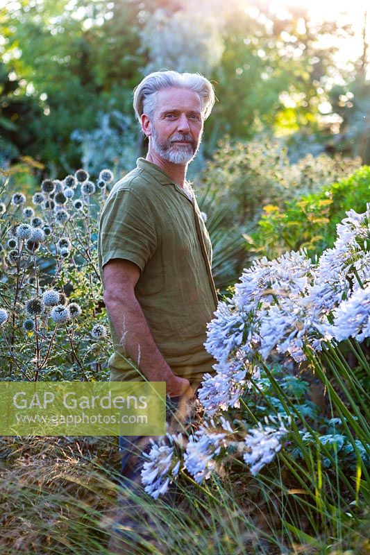 Nick Macer dans le jardin avec Agapanthus 'Windsor Grey' en premier plan, Pan Global Plants, Frampton on Severn, Gloucestershire, Royaume-Uni.