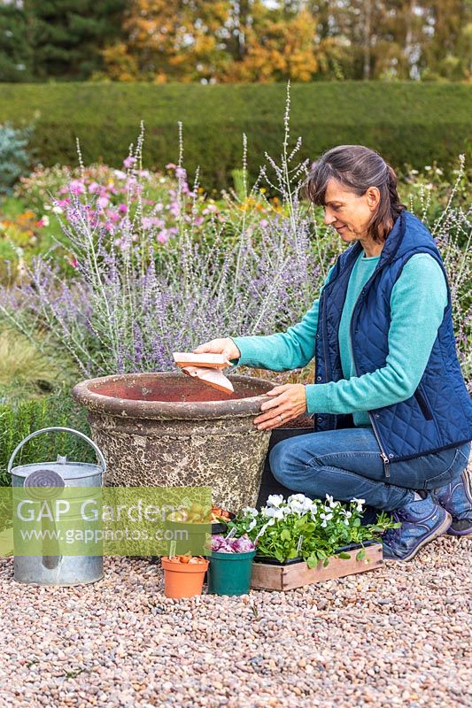 Femme ajoutant des pots au fond du pot pour empêcher le compost de s'écouler à travers les trous de drainage