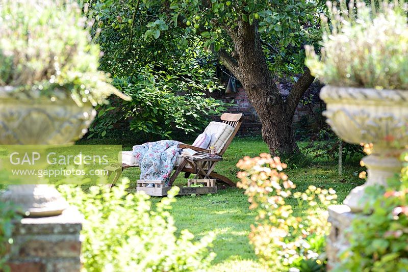 Transat en bois avec coussins et couverture sur pelouse à l'ombre sous un arbre